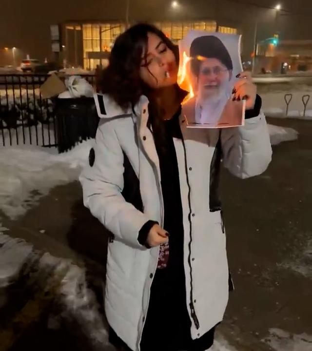 Eine junge Frau zündet ihre Zigarette an einem brennenden Porträt des Obersten Führers des Iran an, Ajatollah Ali Chamenei. 