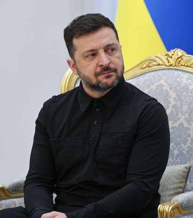 Wolodymyr Selenskyj sitzt vor einer Ukraine-Flagge.