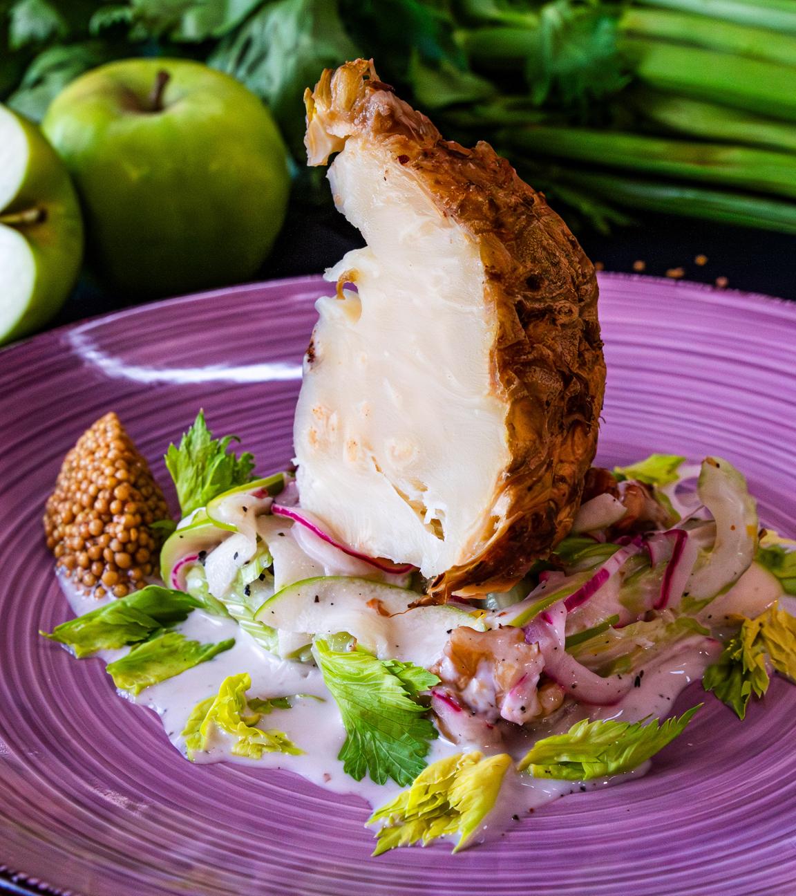 Gebackener Sellerie auf einem violetten Teller mit Waldorf-Salat und Senfkaviar angerichtet.