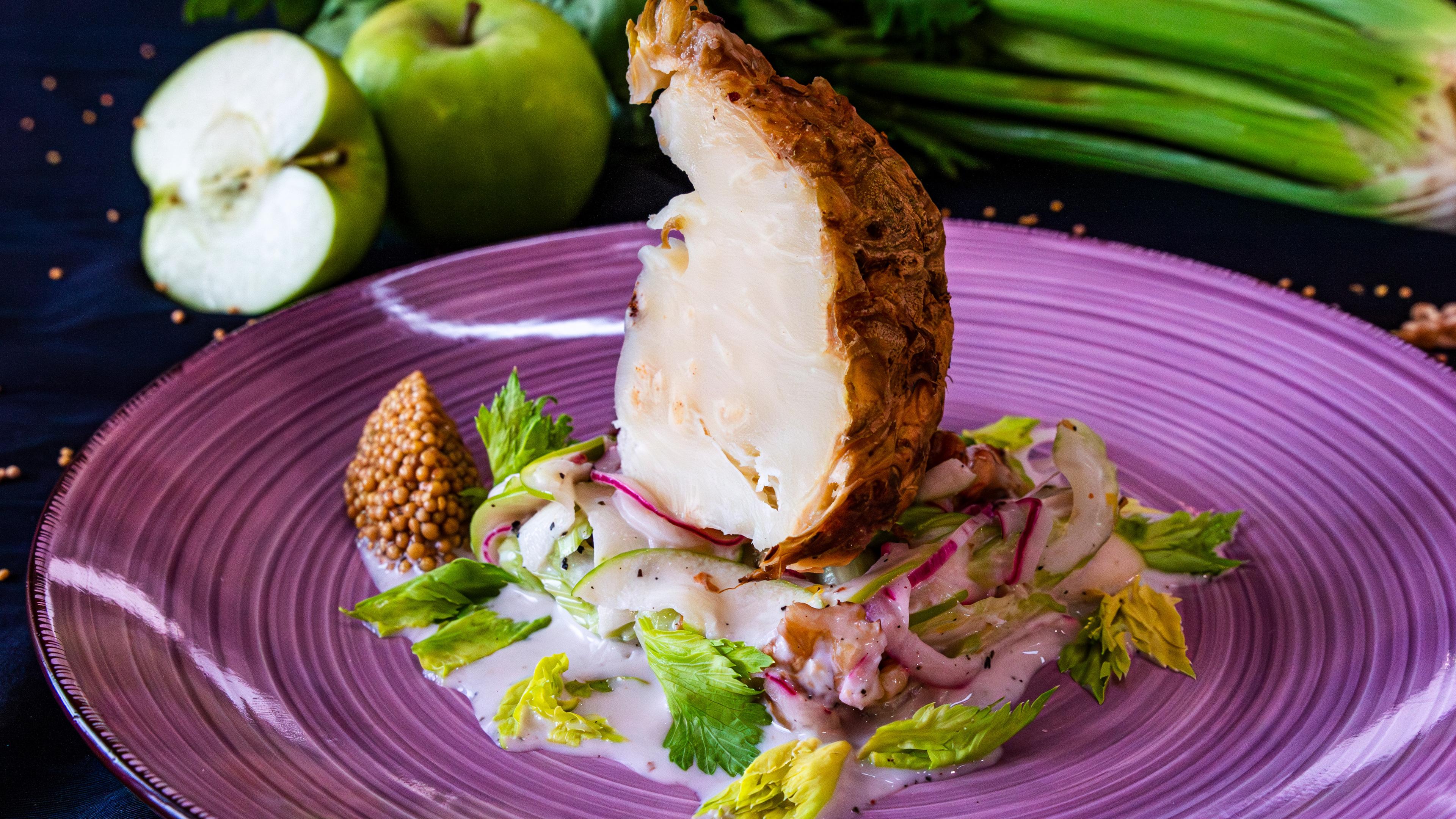 Gebackener Sellerie auf einem violetten Teller mit Waldorf-Salat und Senfkaviar angerichtet.