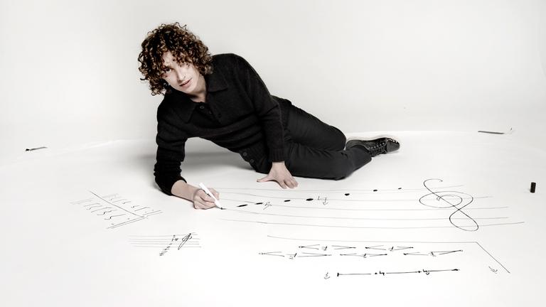 Ein junger Mann liegt auf einem weißen Boden und schreibt mit Edding Noten.