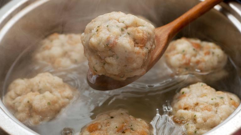 Ein Semmeknödel wird mit einem Kochlöffel aus einem Kochtopf gehoben.