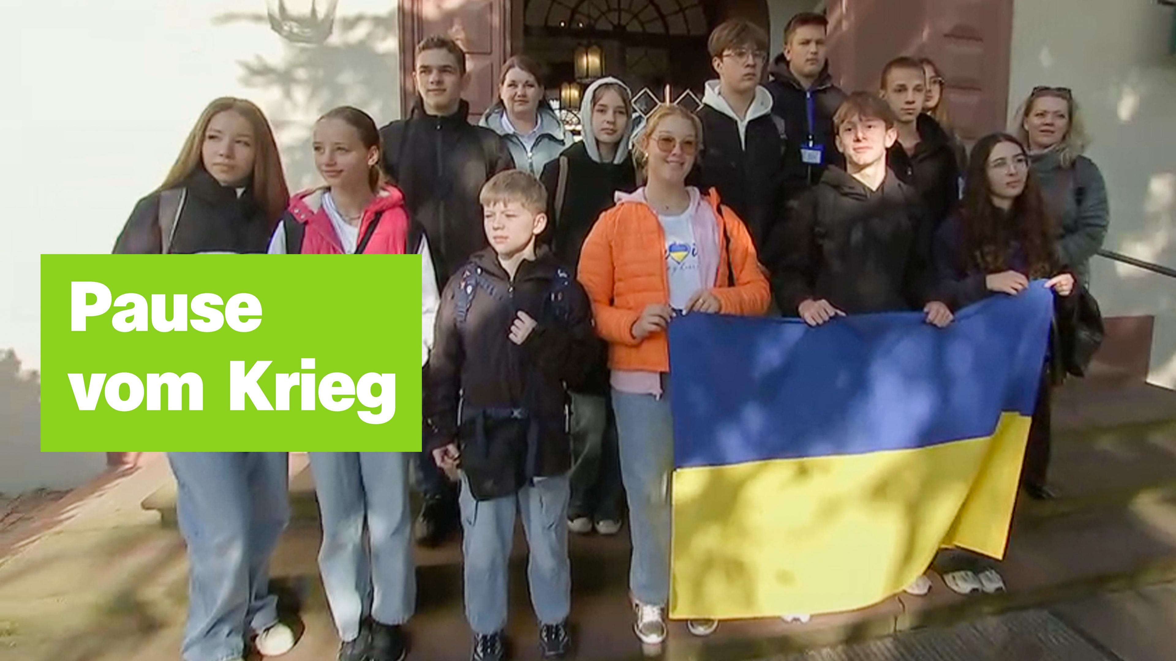 Eine Gruppe von Jugendlichen steht zusammen und hält eine ukrainische Flagge. Links der Text "Pause vom Krieg".