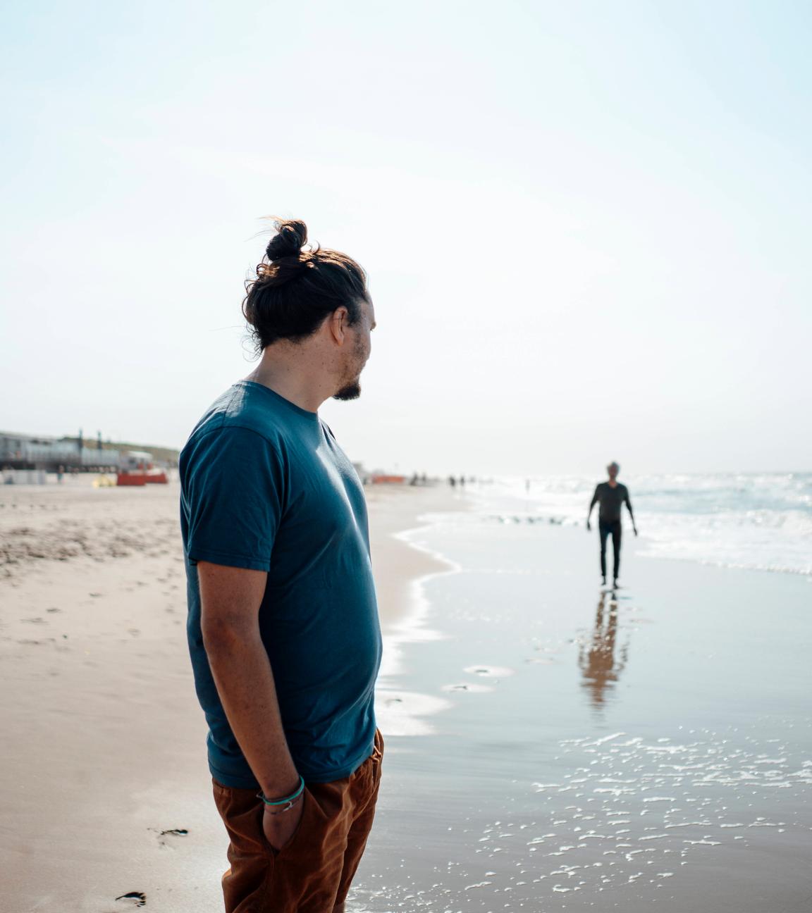 Ein erwachsener Sohn steht an einem Strand und schaut zu seinem Vater in der Ferne.