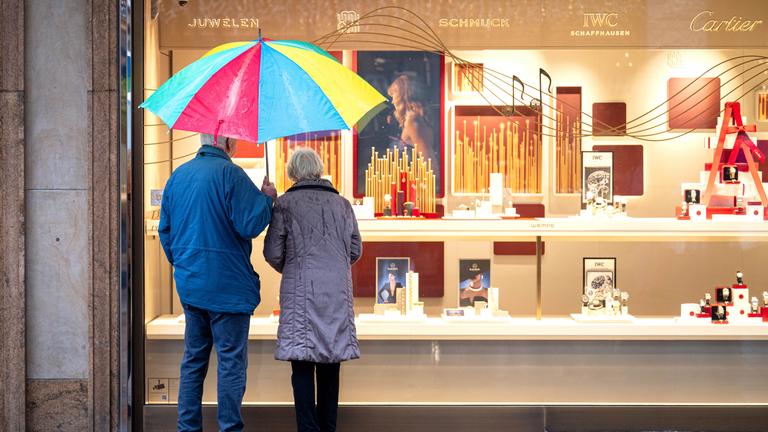 Zwei ältere Personen stehen am 02.12.2025 bei Regen vor einem Schaufenster eines Schmuckgeschäfts in Bremen und betrachten die ausgestellten Waren. 
