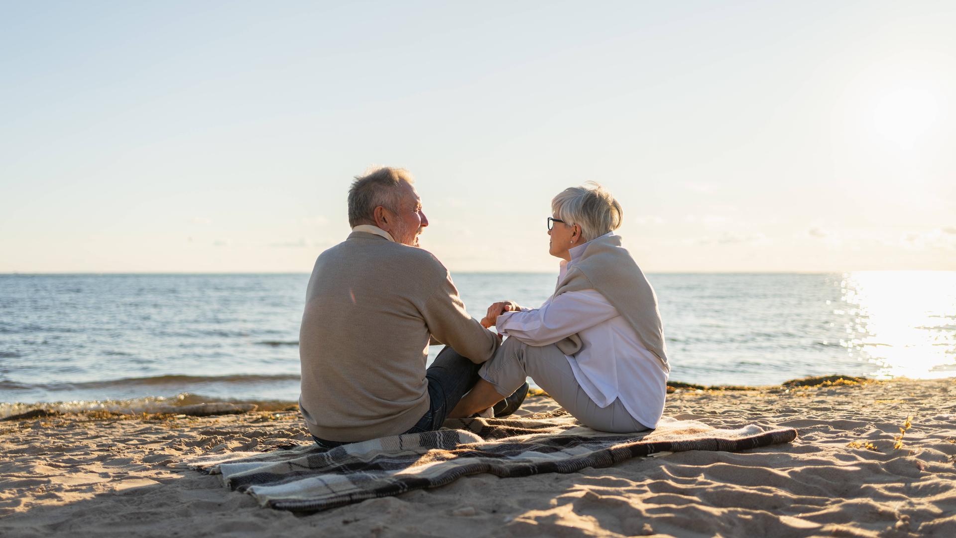 Zwei Senioren sitzen im Sonnenuntergang am Strand.