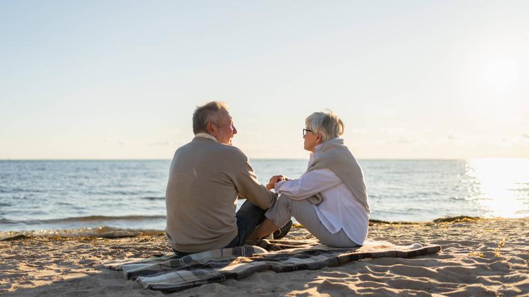 Zwei Senioren sitzen im Sonnenuntergang am Strand.