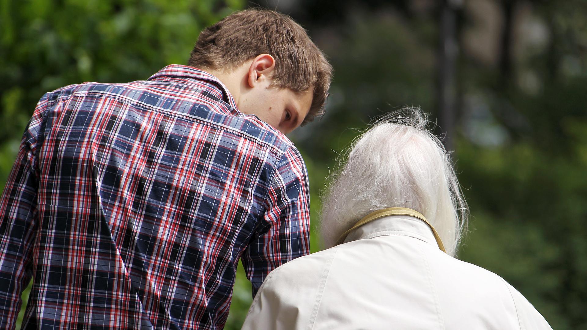 Ein junger Mann begleitet eine alte Frau  (Archivfoto)