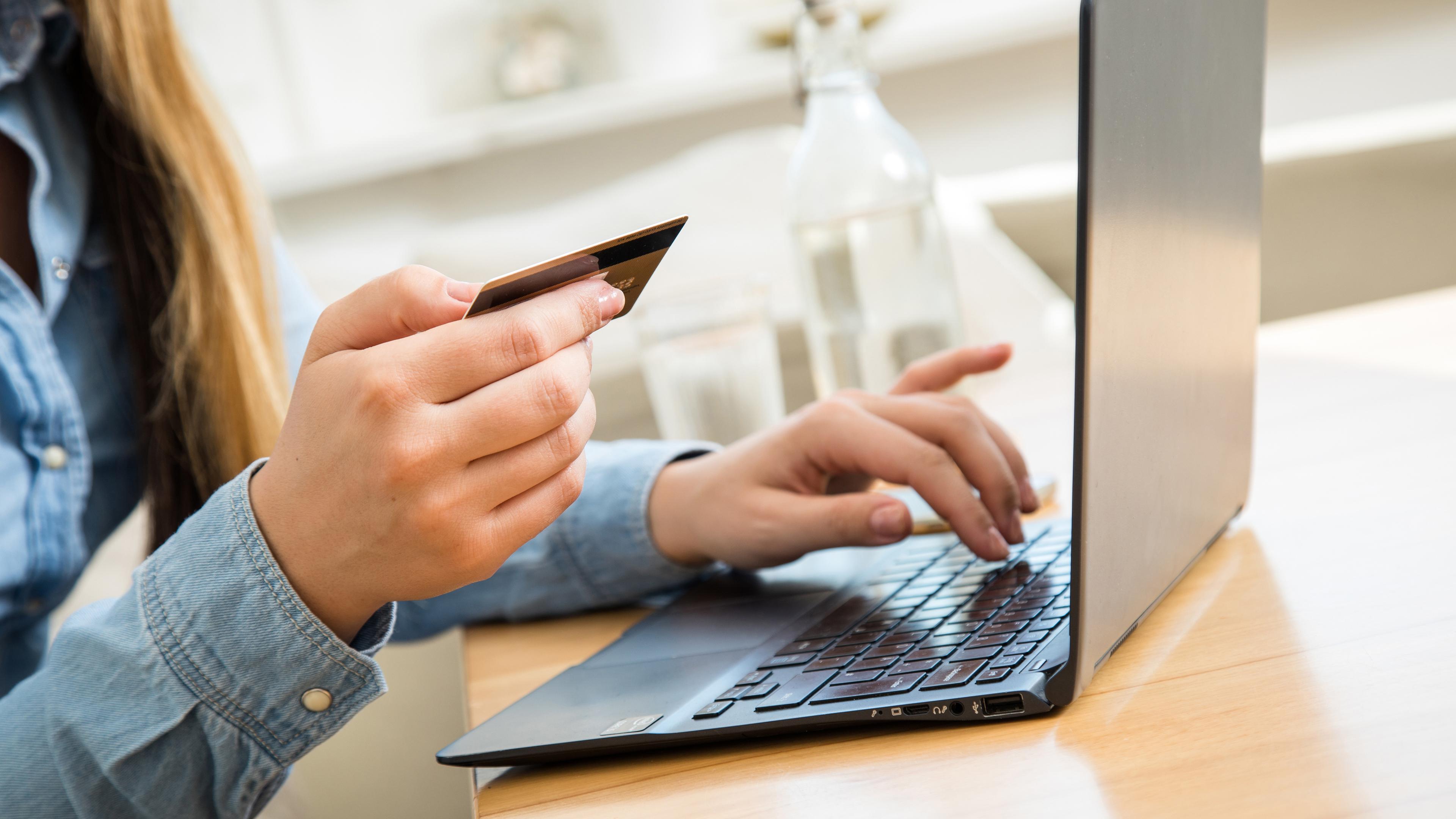 Eine Frau hält eine Karte über einen Laptop, um damit eine Online-Zahlung durchzuführen.