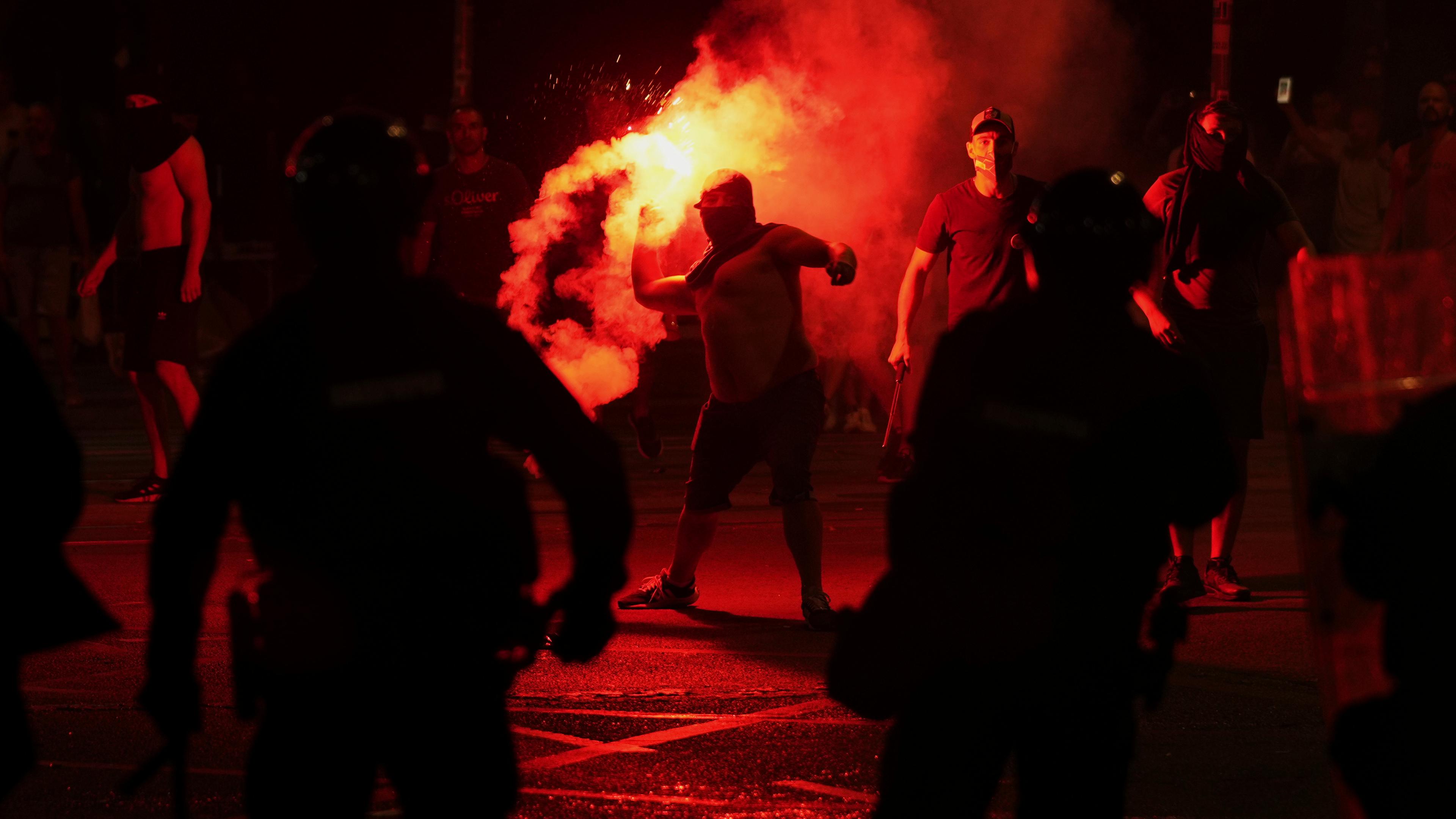 14.08.2025, Serbien, Belgrad: Anhänger des serbischen Präsidenten Vucic werfen während einer Demonstration gegen die Regierung vor dem Büro der serbischen Fortschrittspartei Leuchtraketen auf die Demonstranten.