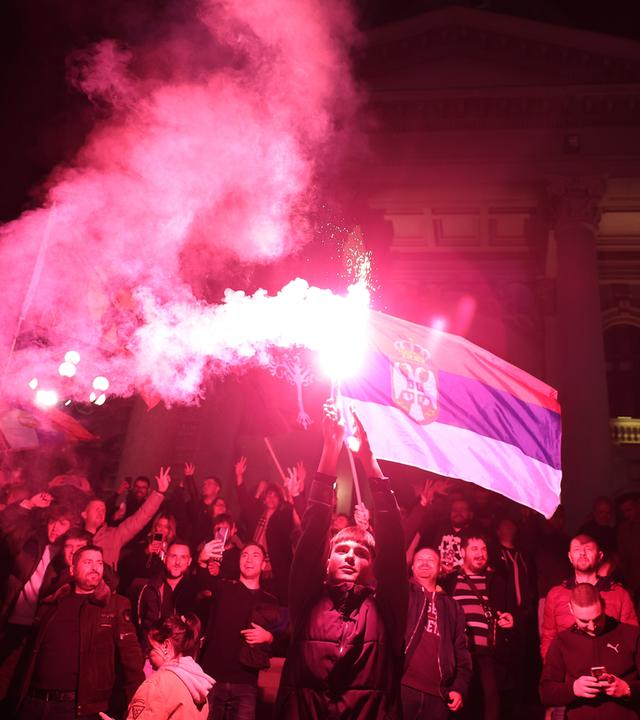 Menschen feiern mit Bengalows und einer Fahne Serbiens vor der Nationalversammlung.