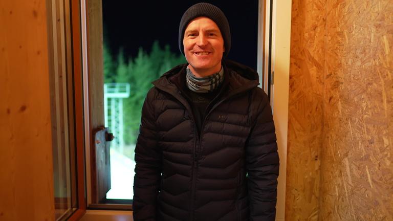 Severin Freund steht mit Mütze und Winterjacke vor einem Fensterrahmen