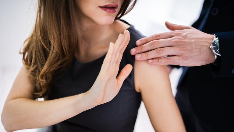 Eine Frau im schwarzen Kleid hält ihre erhobene Hand zur Abwehr gegen die Hand eines Mannes. Beide Gesichter sind nicht zu erkennen.