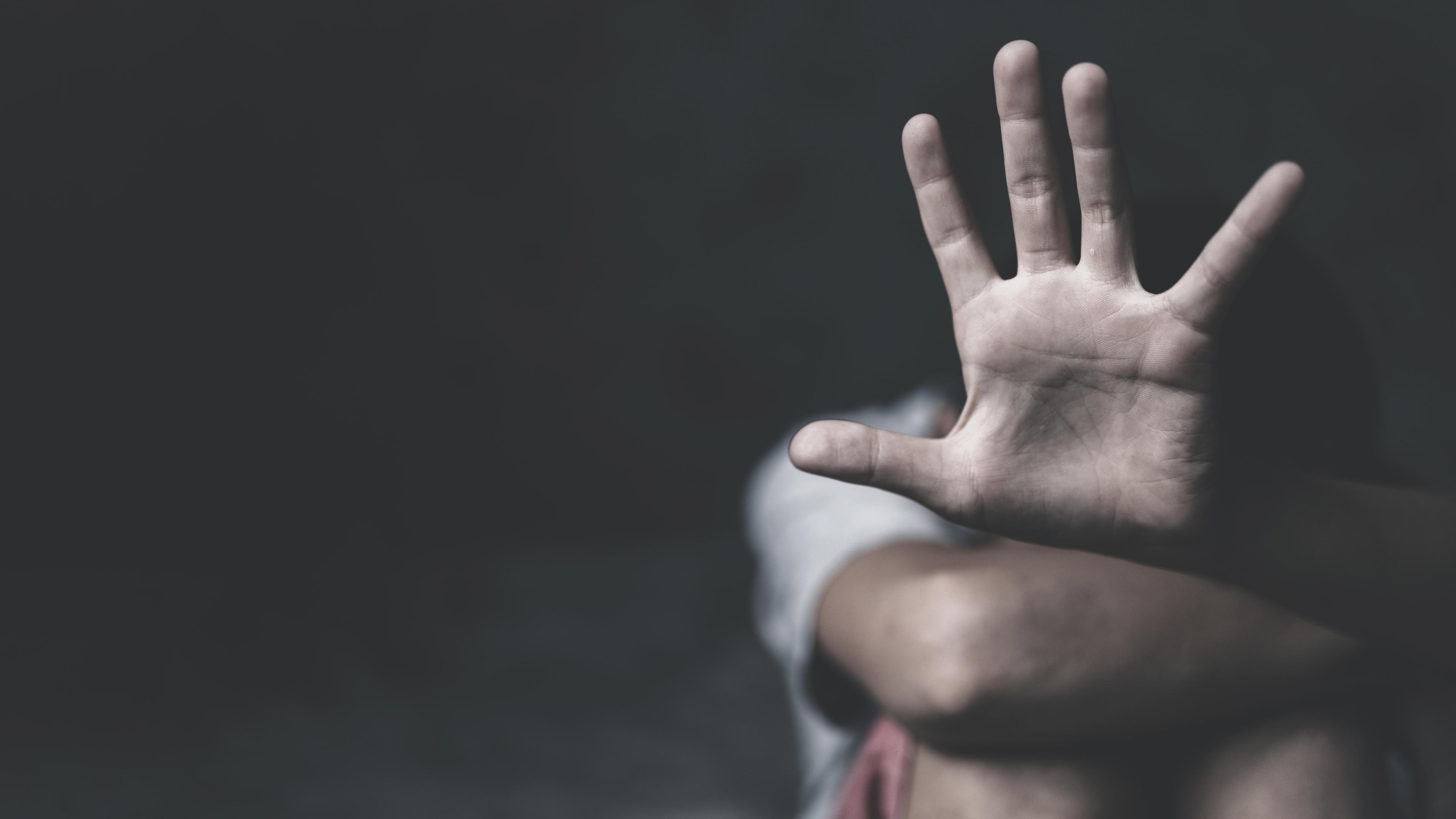 Die offene Handfläche einer kauernden Frau vor schwarzem Hintergrund symbolisiert "Stoppt sexuelle Gewalt an Frauen".