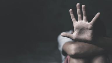 Die offene Handfläche einer kauernden Frau vor schwarzem Hintergrund symbolisiert "Stoppt sexuelle Gewalt an Frauen".
