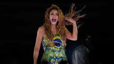 Sängerin Shakira steht lachend auf einer Bühne, sie trägt ein Kleid in grün, gelb und blau - den Nationalfarben Brasiliens.