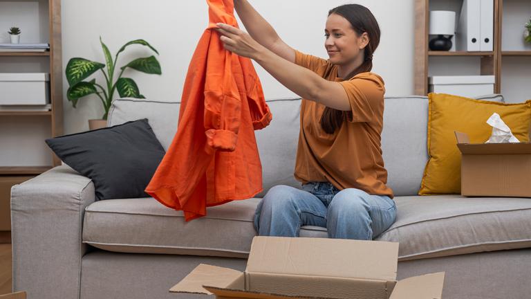 Eine Frau sitzt auf dem Sofa und packt eine Jacke aus einem Paket aus.