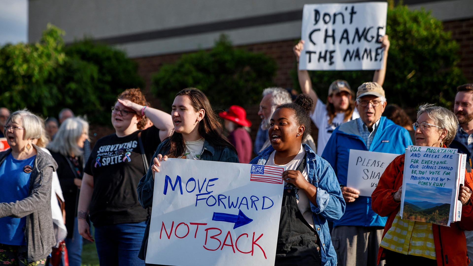 Menschen protestieren mit Plakaten dagegen, dass die Umbenennung der Schule rückgängig gemacht wird.