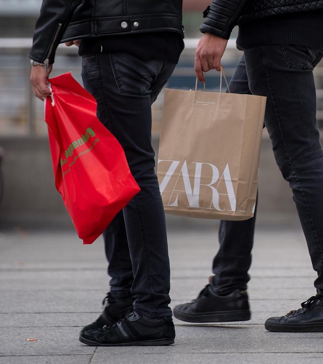 Drei junge Männer mit einkaufstueten gehen über eine Strasse in der Innenstadt.