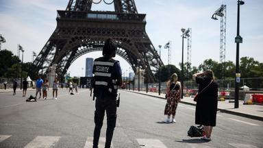 20.07.2024, Frankreich, Paris: Ein Sicherheitsbeamter beobachtet Menschen, die vor dem Eiffelturm fotografiert werden.