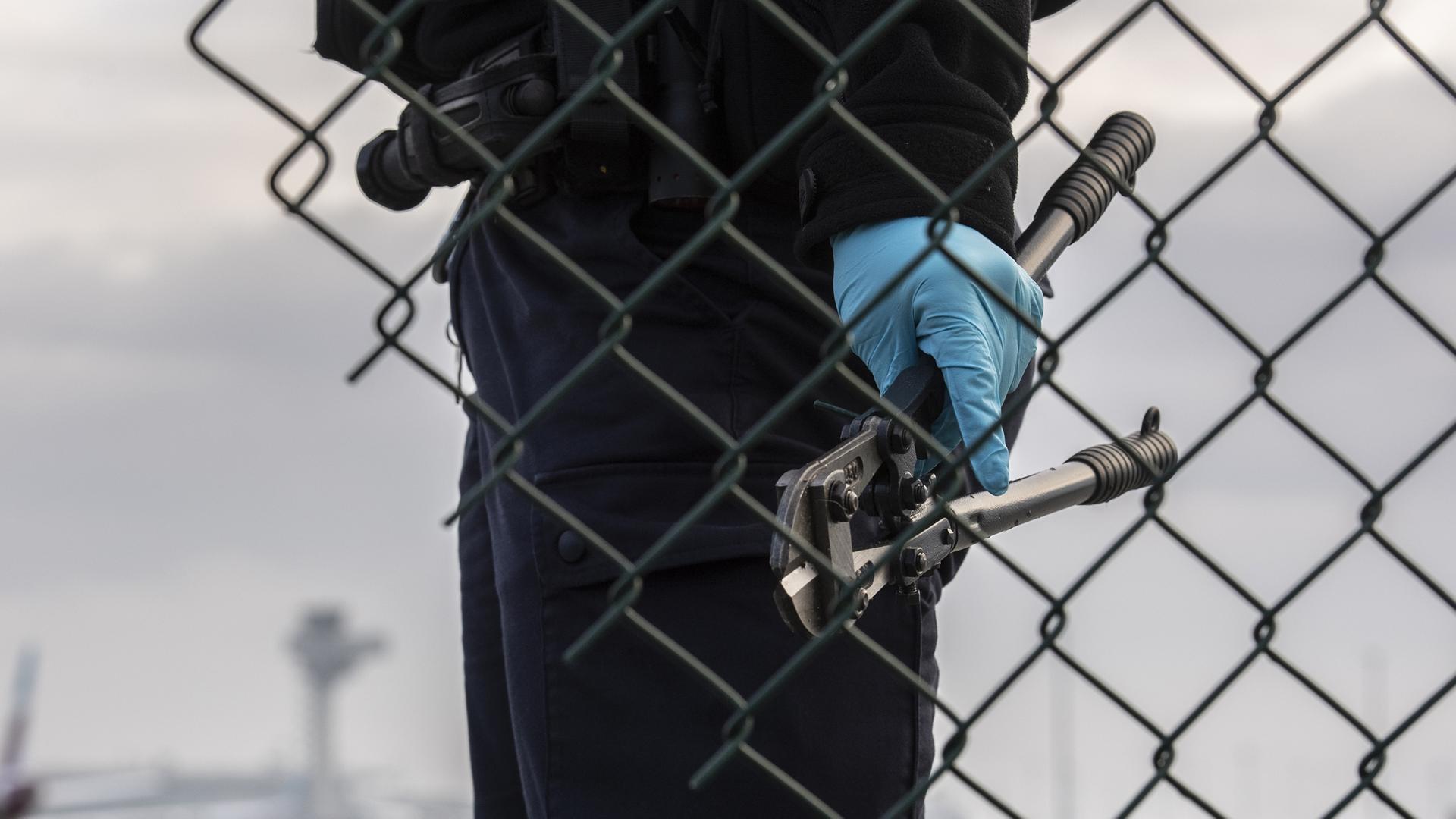 Eine Beamtin der Bundespolizei steht mit einem sichergestellten Bolzenschneider an einem Zaun am BER-Flughafen.