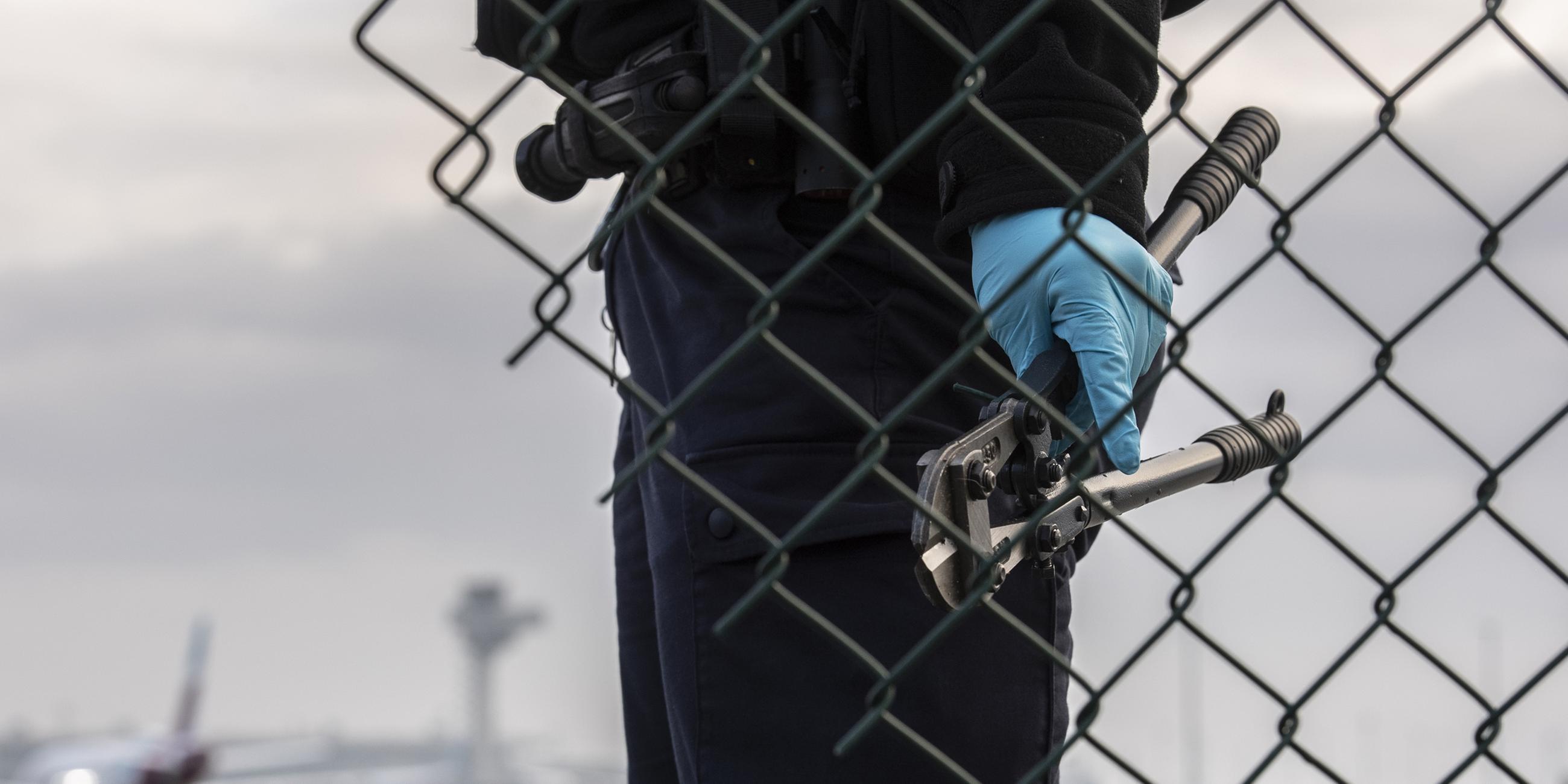 Eine Beamtin der Bundespolizei steht mit einem sichergestellten Bolzenschneider an einem Zaun am BER-Flughafen.