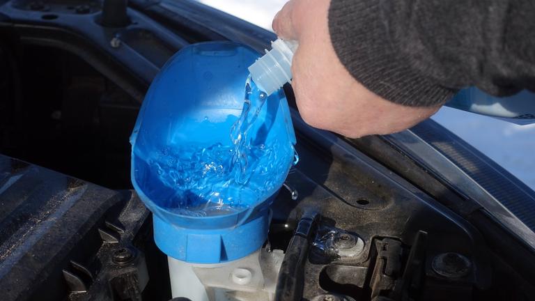 Scheibenreiniger wird in den Tank einer Scheibenwaschanlage im Motorraum eines PKW gegossen. 