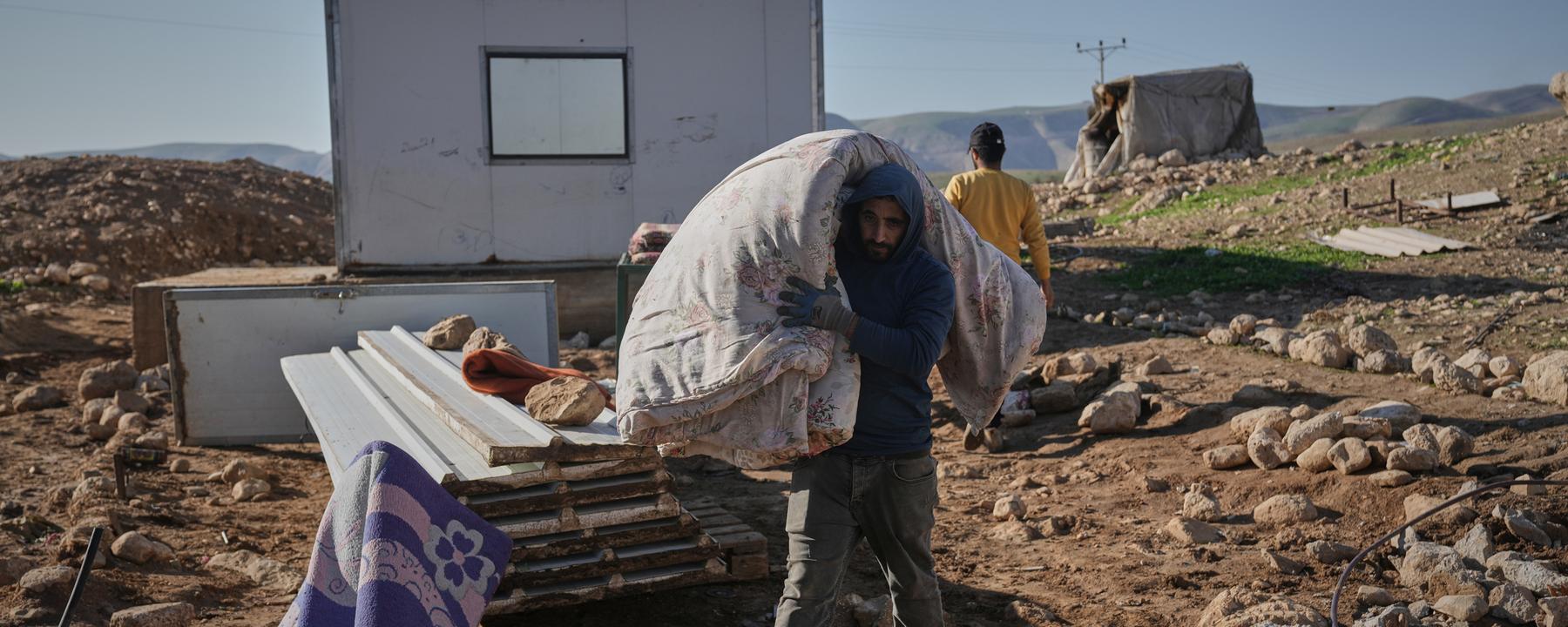 Ein palästinensische Bewohner des Dorfes Ras Ein al-Auja im Westjordanland trägt am 16.01.2026 Bettwäsche auf seiner Schulter, um mit all seinen Habseligkeiten vor der zunehmenden Siedlergewalt zu fliehen.