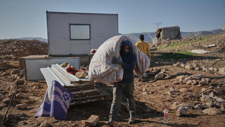 Ein palästinensische Bewohner des Dorfes Ras Ein al-Auja im Westjordanland trägt am 16.01.2026 Bettwäsche auf seiner Schulter, um mit all seinen Habseligkeiten vor der zunehmenden Siedlergewalt zu fliehen.