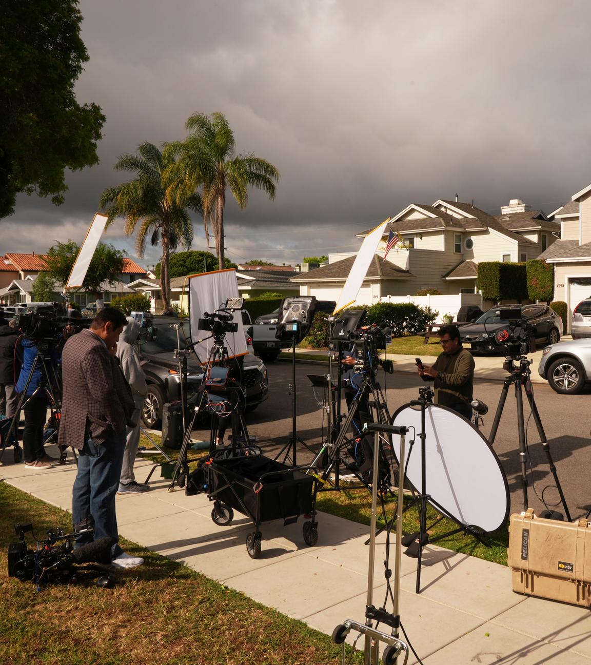 Medienvertreter stehen mit Kameras in einem Wohngebiet am Rand einer Straße.