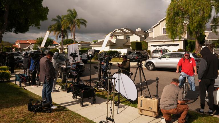 Medienvertreter stehen mit Kameras in einem Wohngebiet am Rand einer Straße.