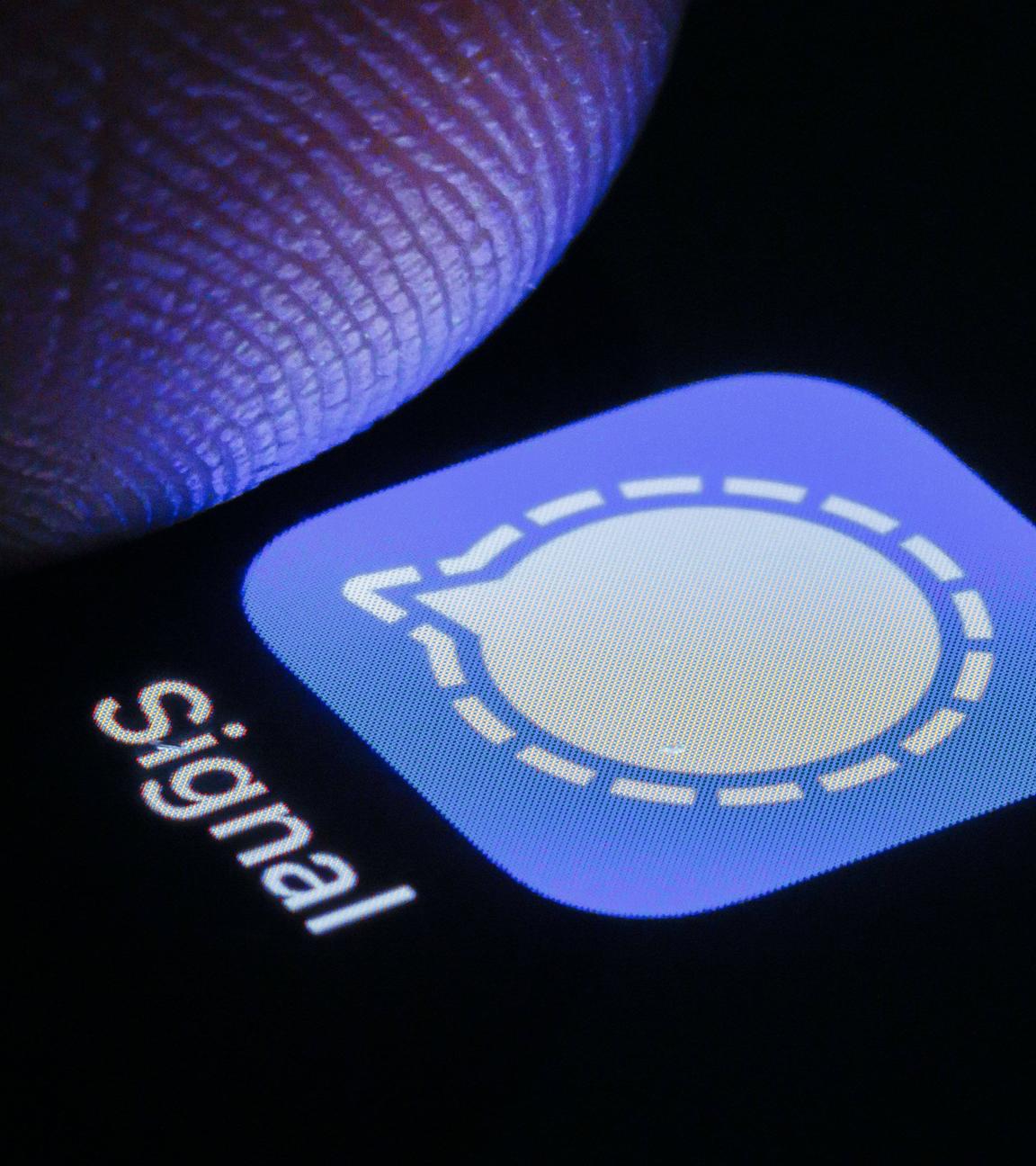 Die App von Signal ist auf deinem Smartphone neben einem Finger zu sehen.