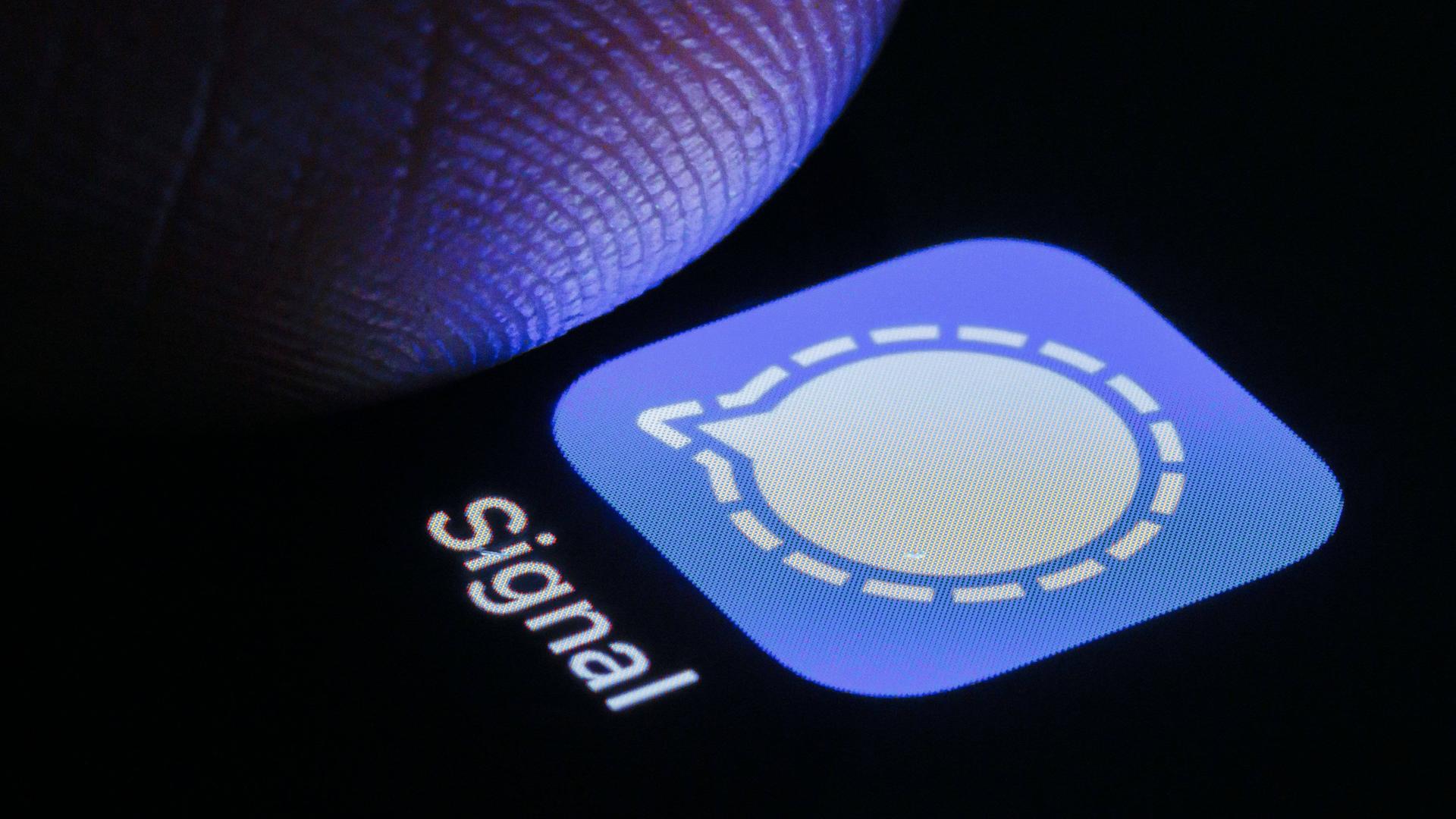 Die App von Signal ist auf deinem Smartphone neben einem Finger zu sehen.