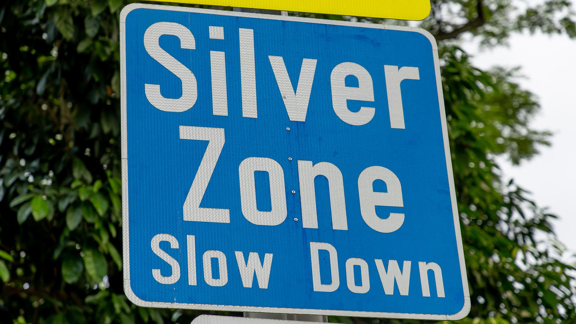 Auf einem blauen Straßenschild mit weißer Aufschrift steht: Silver Zone, Slow down.