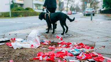 Mann geht mit Hund Gassi vorbei an abgebrannten Silvesterraketen