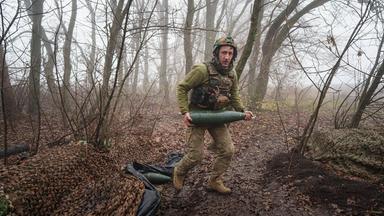 Ein ukrainischer Soldat des Bataillons Da Vinci Wolves trägt eine Artilleriegranate, bevor er auf russische Stellungen an der Frontlinie in der Ostukraine feuert. 