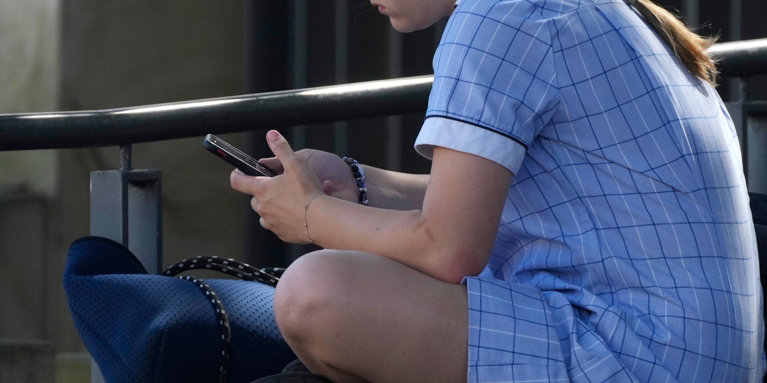 Ein junges Mädchen sitzt mit dem Handy in der Hand auf einer Bank in Sydney.