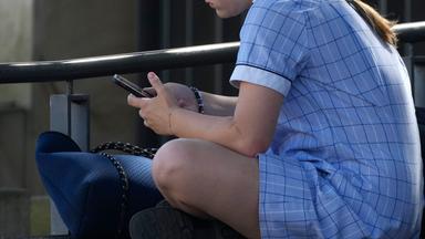 Ein junges Mädchen sitzt mit dem Handy in der Hand auf einer Bank in Sydney.