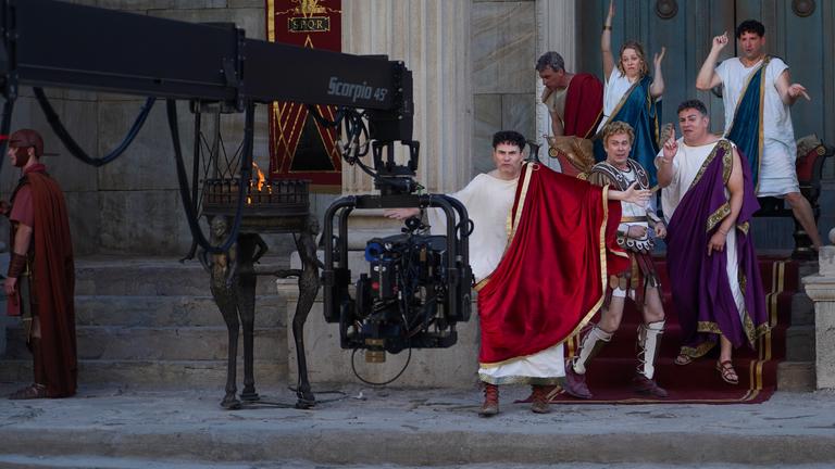 Auf den Treppen vor einem Eingangsportal zu einem großen Gebäude stehen Alexander Schubert, Paul Sedlmeir, Jasmin Schwiers, Matthias Matschke und Carsten Strauch. Sie alle haben beim Tanzen unterschiedliche Posen eingenommen. Vor ihnen ragt ein Kameraarm ins Bild, neben ihnen stehen Feuerschalen.