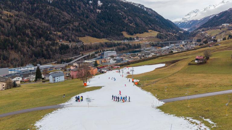 Skifahrer auf einem schmalen Streifen künstlichem SChnee in den Schweizer Alpen.