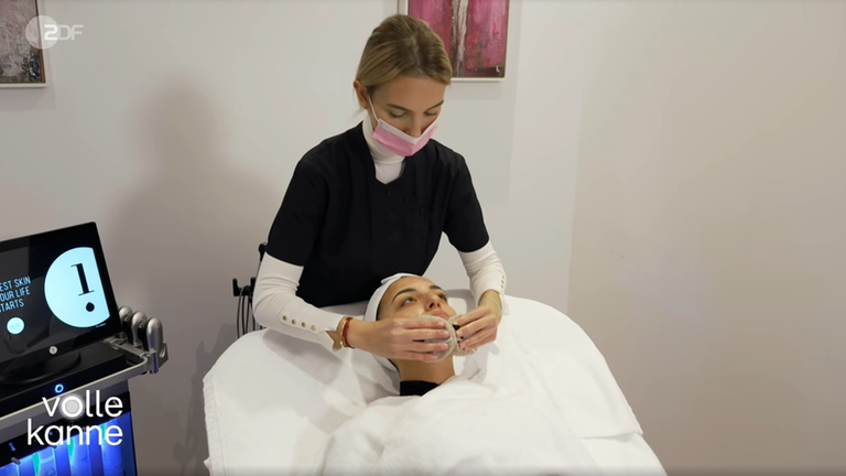 Kosmetikerin trägt Creme auf Gesicht einer Frau auf