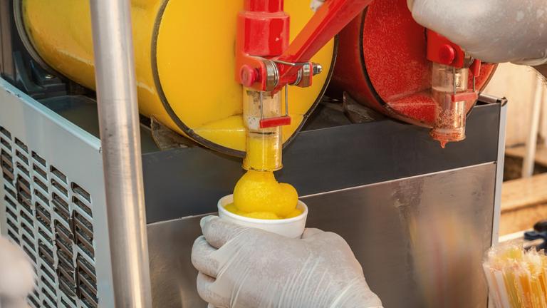 Ein Verkäufer zapft Slush-Eis aus einer Maschine in einen Trinkbecher ab.