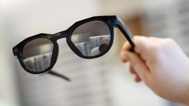Symbolbild:  Eine Frau hält in einem Brillenfachgeschäft eine smarte Datenbrille