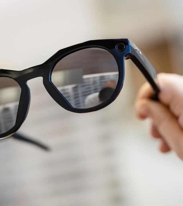Symbolbild:  Eine Frau hält in einem Brillenfachgeschäft eine smarte Datenbrille