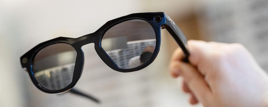 Eine Hand hält eine smarte Datenbrille in einem Geschäft hoch.