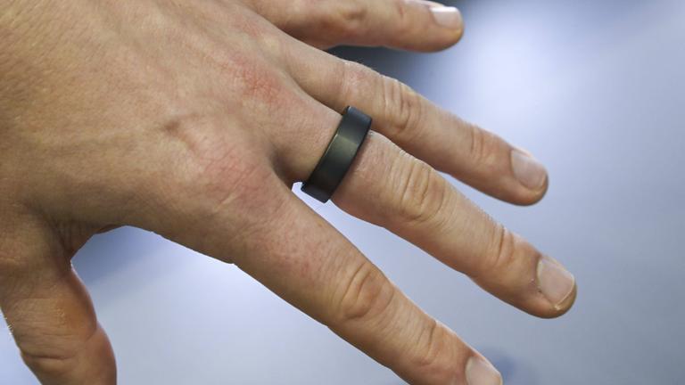 Nahaufnahme einer Hand, die einen Smart-Ring am Zeigefinger trägt. Der Ring ist schlicht und metallisch.