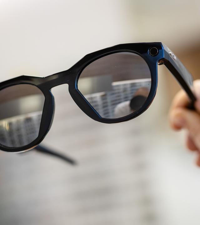  Eine Frau hält in einem Brillenfachgeschäft eine smarte Datenbrille der Firma Oakley Meta in ihrer Hand.