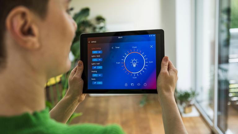Eine Frau mit einem Tablet in der Hand steuert ihr Smarthome-System für Licht.