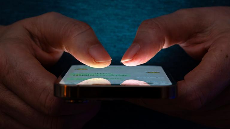 Symbolbild: Frau tippt auf einem Apple iPhone13 Smartphone-Screen SMS