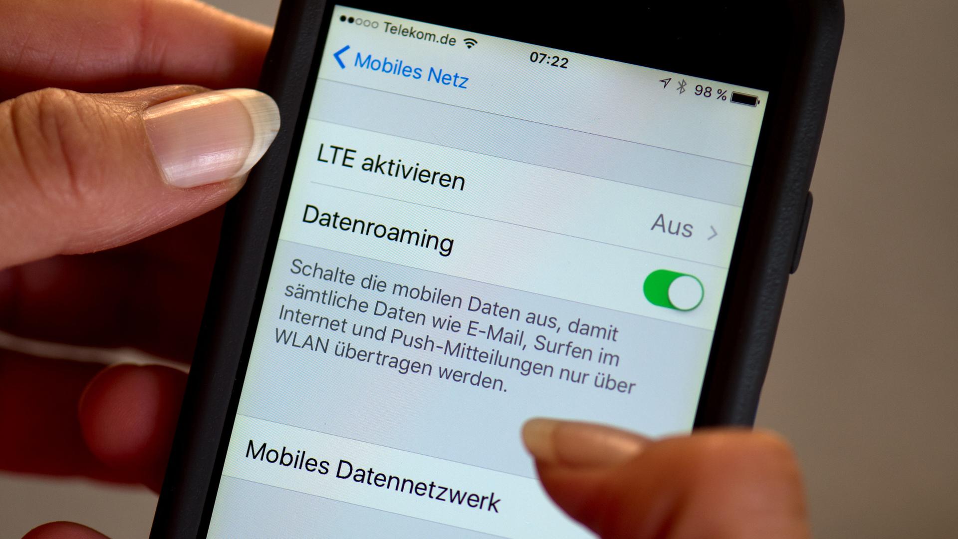 Eine Hand hält ein Smartphone. Darauf sind die Einstellungen für das Datenroaming und mobile Daten zu sehen.